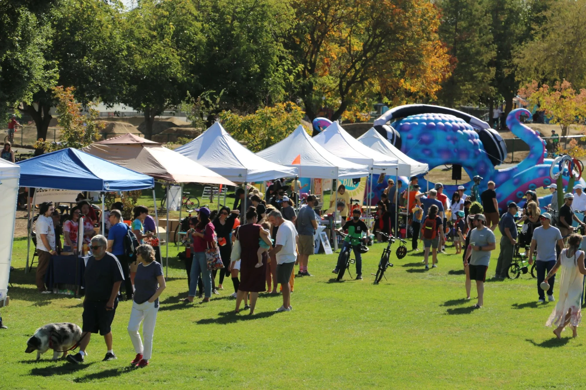 Festival goers browse a row of sponsor tents beside a giant inflatable octopus mascot.