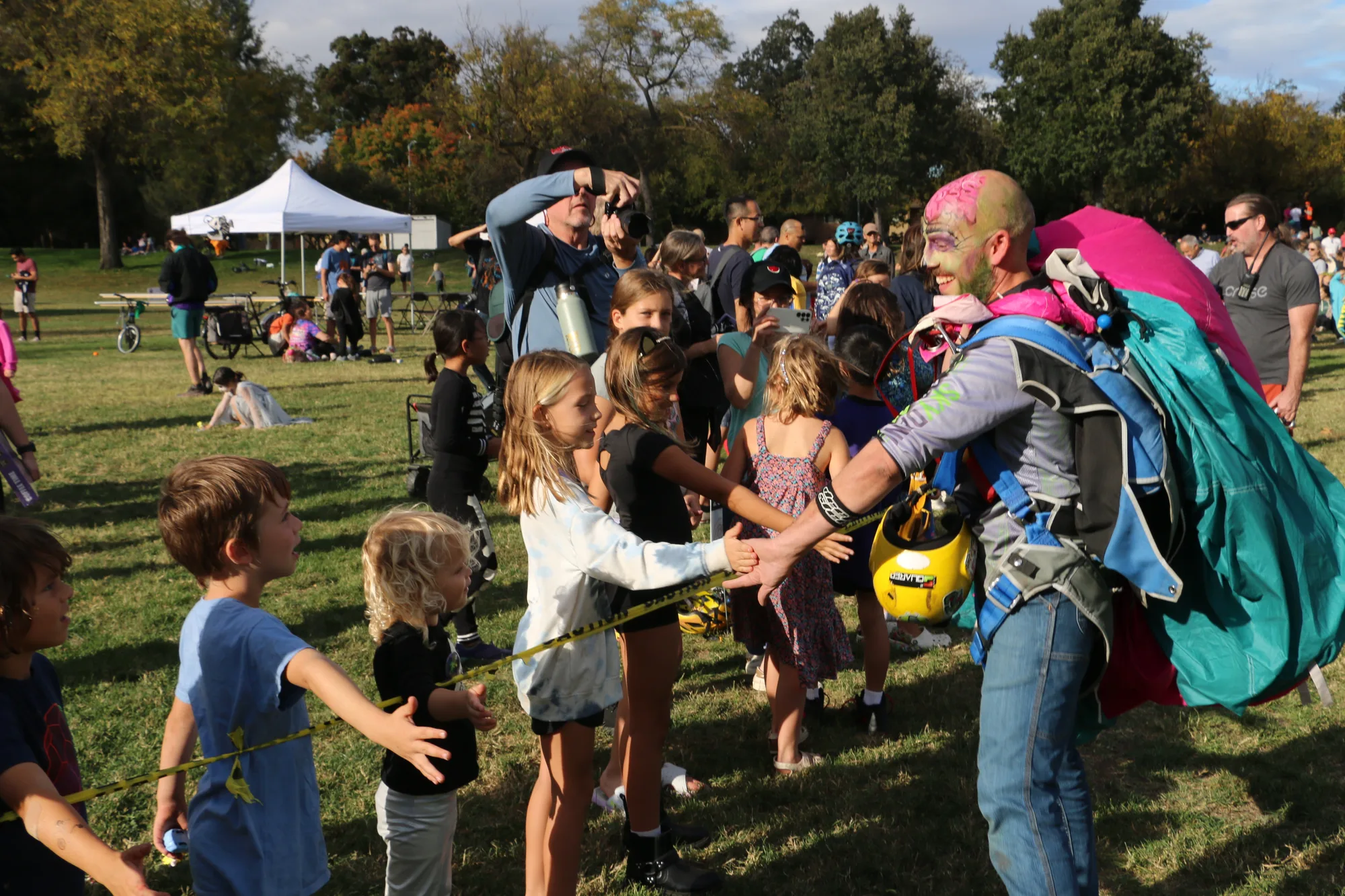 A skydiver in zombie makeup high-fives a line of excited kids after landing.